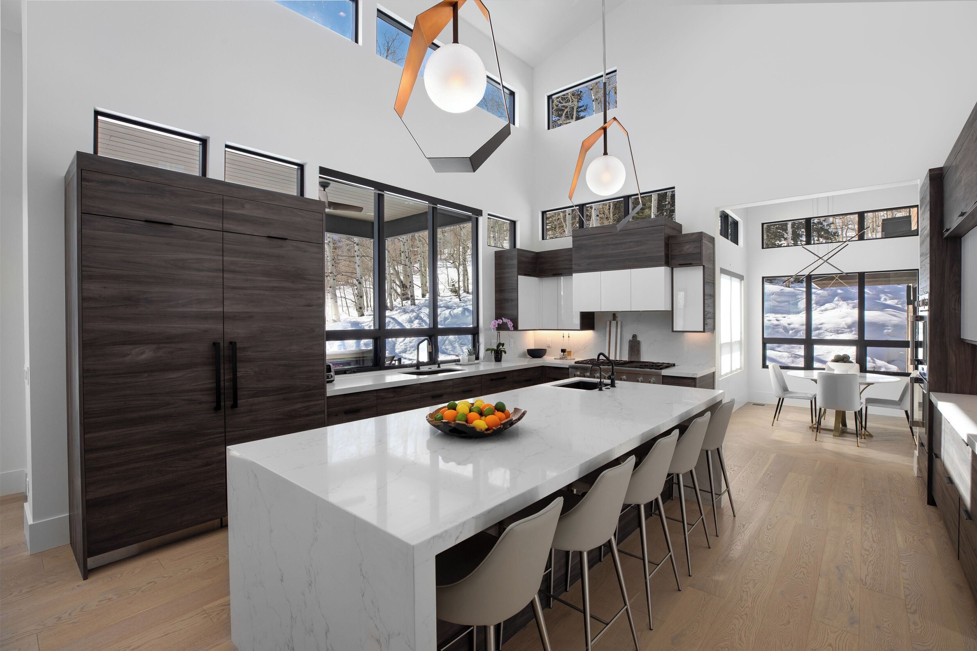Una cocina moderna con una isla grande, armarios de madera oscura y vistas a un paisaje nevado a través de amplios ventanales.