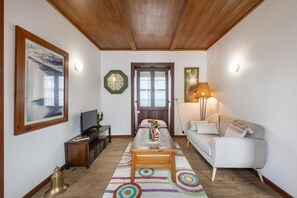 A living room with a wooden ceiling, a sofa, a television, a coffee table, a rug, and a door with windows.