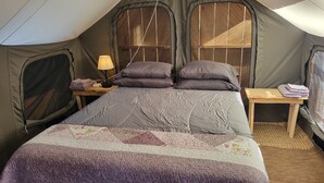 Une tente équipée d’un lit, de deux tables de chevet et d’une lampe.