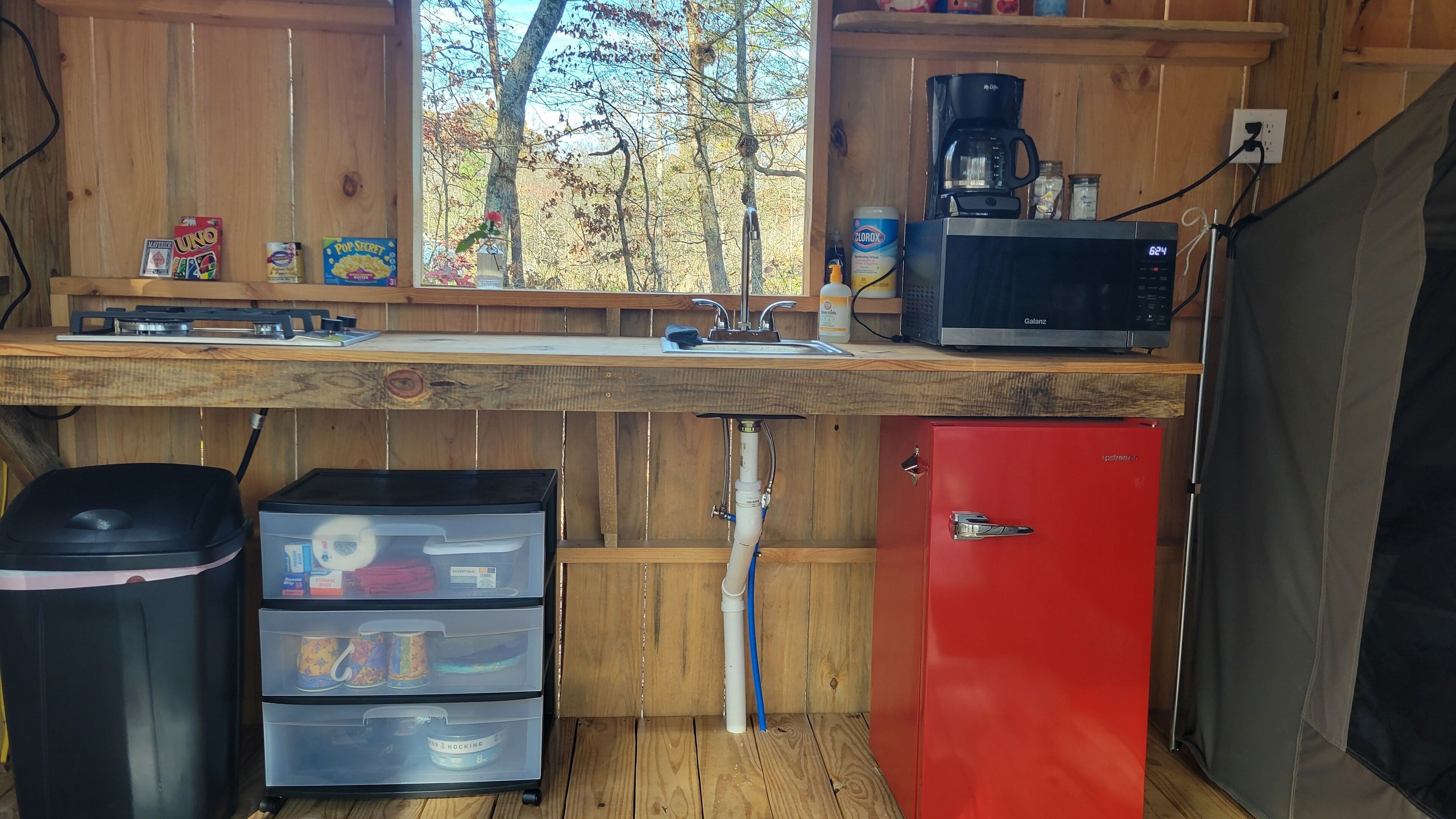 A compact kitchen with a sink, a coffee maker, and a red refrigerator.