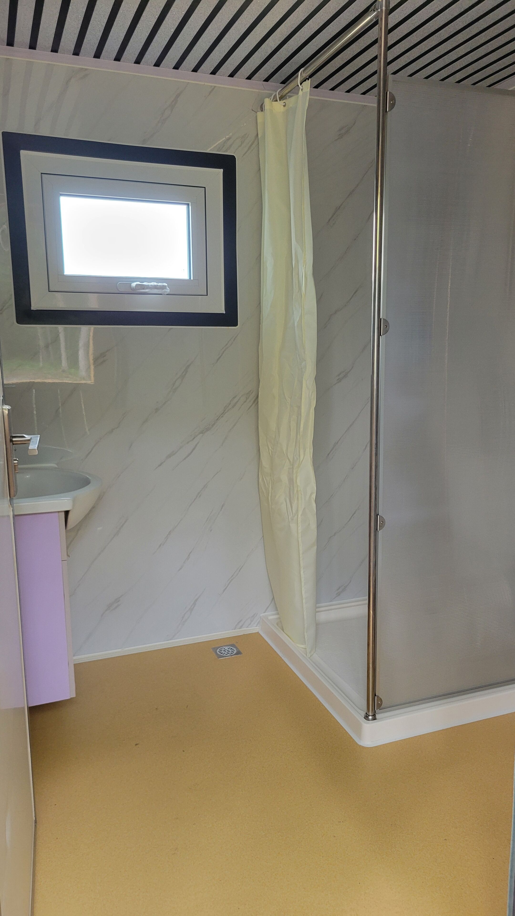Ein Badezimmer mit Dusche, Waschbecken und Fenster.