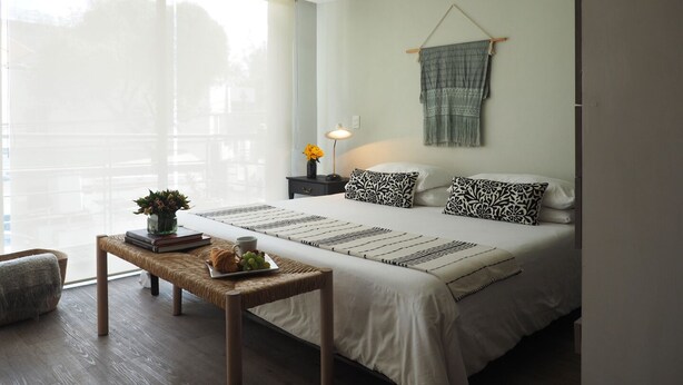 A modern bedroom with a large bed, bedside tables, a bedside lamp, and a view through a large window.