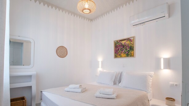 Een hotelkamer met een bed, nachtkastje, spiegel, airconditioning en een wandlamp.