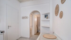 Een gang met een witte deur, een glazen tafel met onderzetter en een plankje met decoratieve objecten.