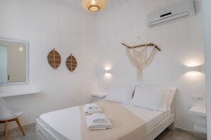 A bedroom with a bed, bedside table, wall-mounted air conditioner, decorative wall art, and a hanging macrame piece.