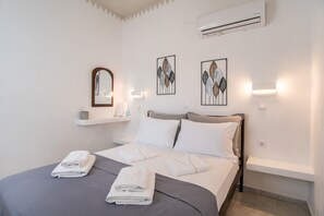 A neatly made bed with white linens and towels, a bedside table with a lamp, and wall-mounted artwork.