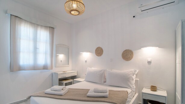 A hotel room with a bed, bedside tables, a mirror, and a hanging light fixture.