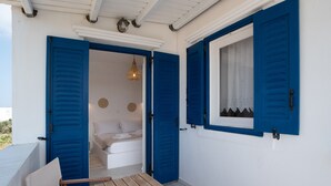 A room with a bed, a table, and a window with blue shutters.