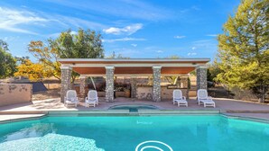 A swimming pool with a stone border, white lounge chairs, and a pergola structure. - Vineyard Vista Retreat– Your Serene Getaway in Temecula (Temecula)