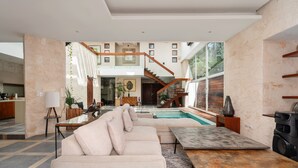 Un amplio salón con piscina, una escalera y una cocina moderna al fondo.