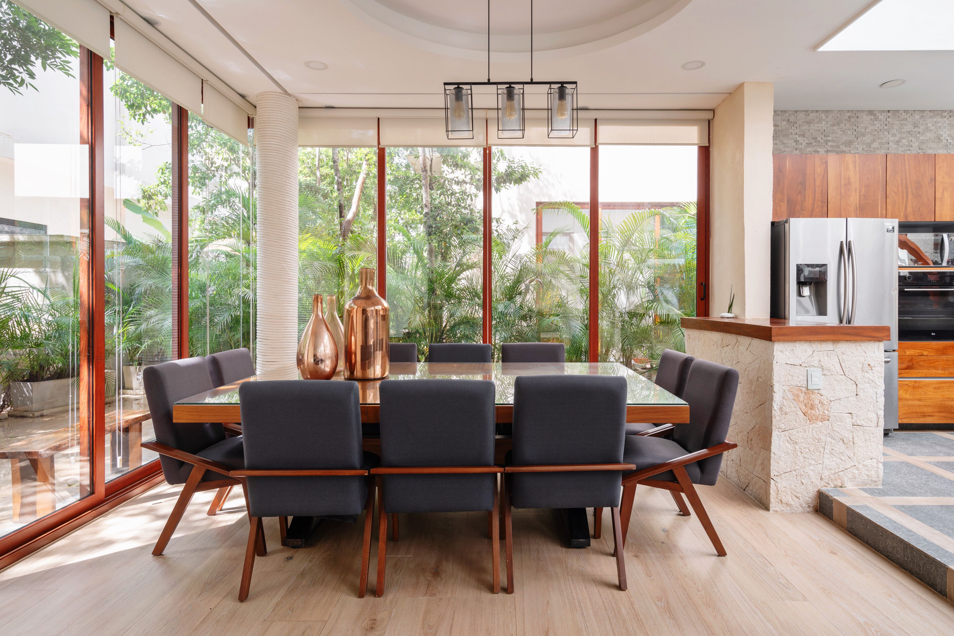 Een moderne eetruimte met een glazen tafel en stoelen, een keuken met houten keukenkastjes, en uitzicht op groen buiten.