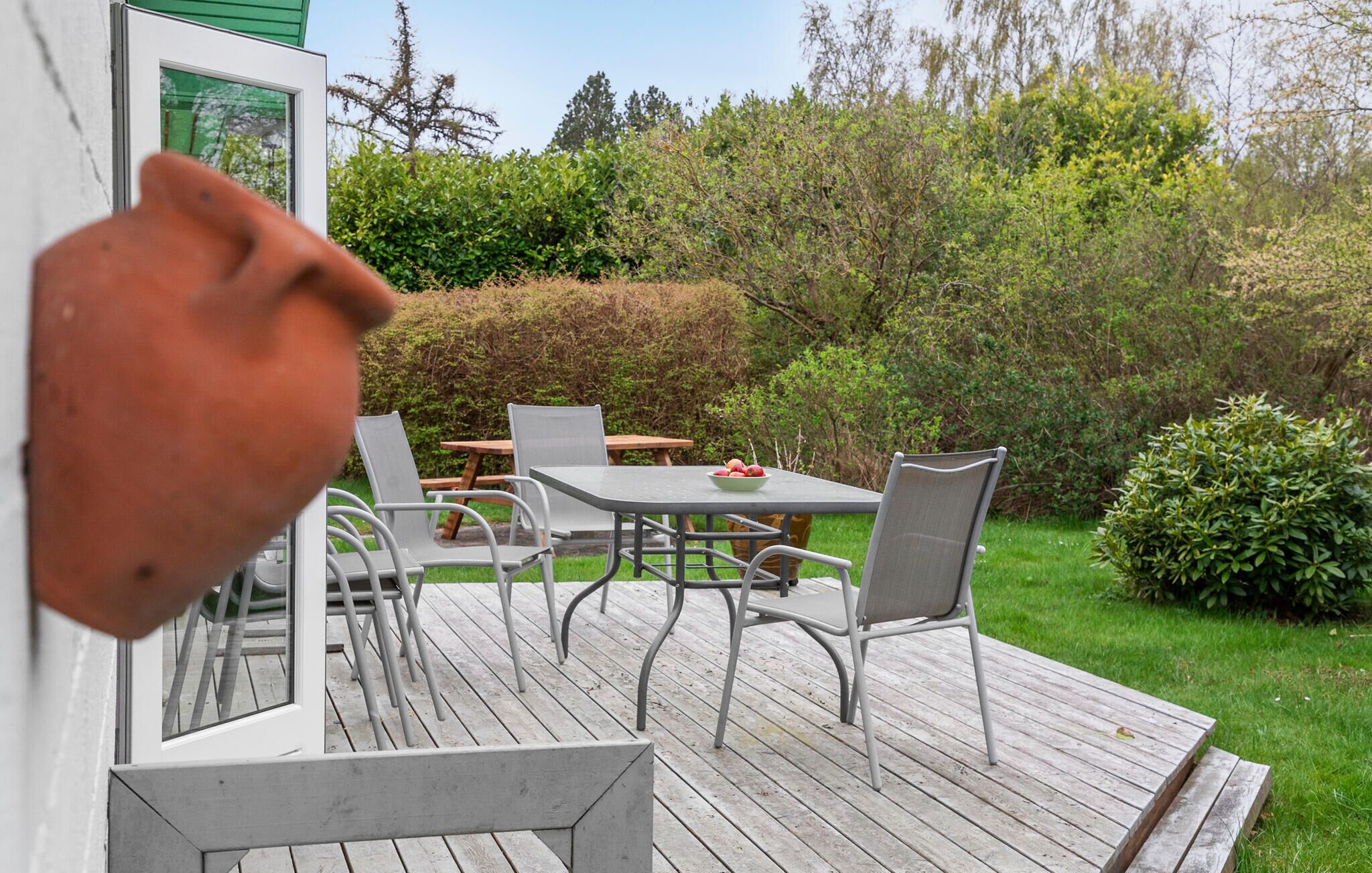 Een terras buiten met een tafel, stoelen, een potplant en uitzicht op een tuin.