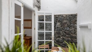 A small, enclosed outdoor area with a stone wall, a wooden table with a book and a cup, and a chair. - Holiday Home 'Casa Princesa Guayarmina 49' with Private Terrace, Garden & Wi-Fi (Puerto del Carmen)