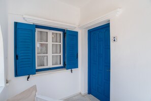 Une pièce avec un mur blanc, une fenêtre avec des volets bleus et une porte bleue.