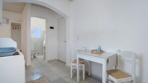 A white room with a glass table, two chairs, a small window, and a door leading to a bathroom.