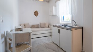 Eine kompakte Küche mit Essbereich, einer Pendelleuchte, einem Fenster mit Vorhängen und einem an der Wand befestigten Schrank.