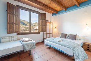 A bedroom with a bed, a bench, a radiator, a window with wooden shutters, and a view of hills. - Country House 'Casona Y Posada' with Mountain View, Wi-Fi and Air Conditioning (Chera)