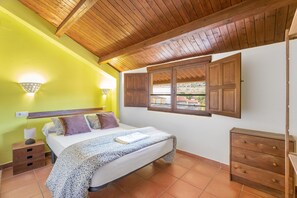 A bedroom with a bed, wooden ceiling, a window with shutters, a nightstand, and a dresser.