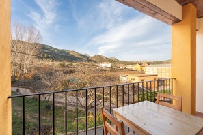 A balcony with a view of a valley, a table, and chairs.