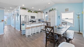 Una cocina moderna con armarios blancos, una isla central con taburetes de bar, electrodomésticos de acero inoxidable y vistas al área de comedor.