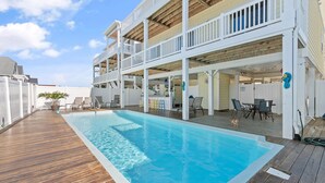 Una piscina con cubierta de madera, una zona de estar techada al aire libre y un edificio de varios niveles con balcones.