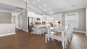 A spacious kitchen with white cabinetry, a central island with stools, and a dining area with a large table and chairs. - "Marina Jack" 5 Bedroom 5 Bath with a Pool! (Holden Beach)