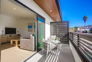 A modern balcony with a sofa, chairs, and a table, overlooking a residential area.
