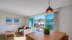 A modern living room with a wooden dining table, a sofa, and a balcony with a view of the city.