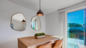 Un coin repas avec une table en bois, deux chaises, un luminaire suspendu et une grande fenêtre donnant sur un paysage.
