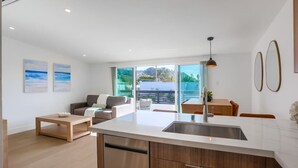 Eine moderne Küche mit einer zentralen Kochinsel, einem Essbereich mit Tisch und Stühlen, einem Sofa und einem großen Fenster mit Aussicht.