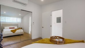 Ein Schlafzimmer mit einem großen Spiegel, einem Bett mit gelber Decke, einem hölzernen Korb mit Tassen und einer weißen Tür.
