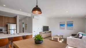 Eine moderne Küche mit Kochinsel, ein Essbereich mit Tisch und Stühlen sowie ein Wohnzimmer mit Sofa und Fernseher.