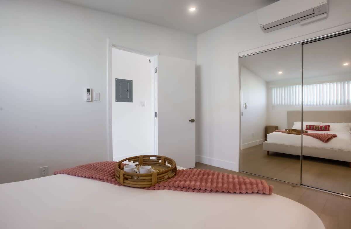 A modern bedroom with a bed, a bedside table, a mirror, and a sliding door leading to another room.