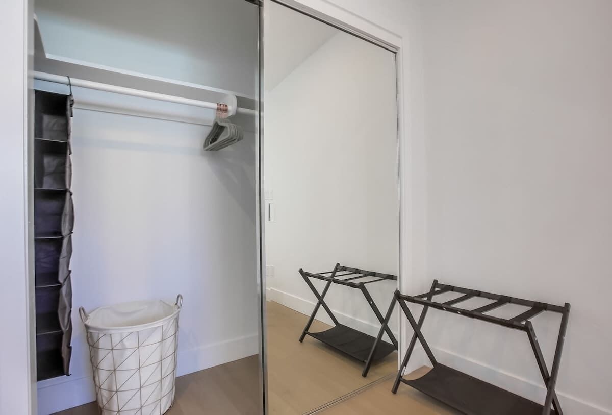 A closet with a hanging rod, a storage bin, and a mirror.