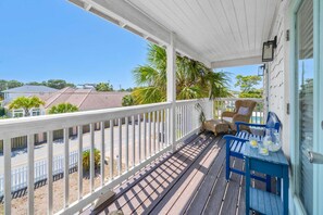 A covered porch with a white railing, a table with chairs, and a view of houses and palm trees.