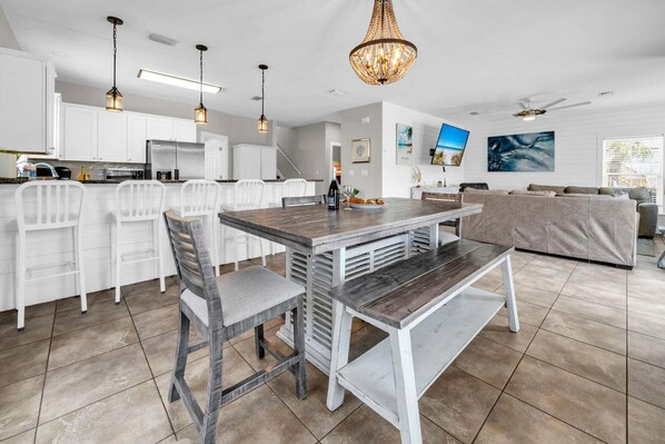 A modern kitchen with white cabinets, a dining table with chairs, and a large chandelier.