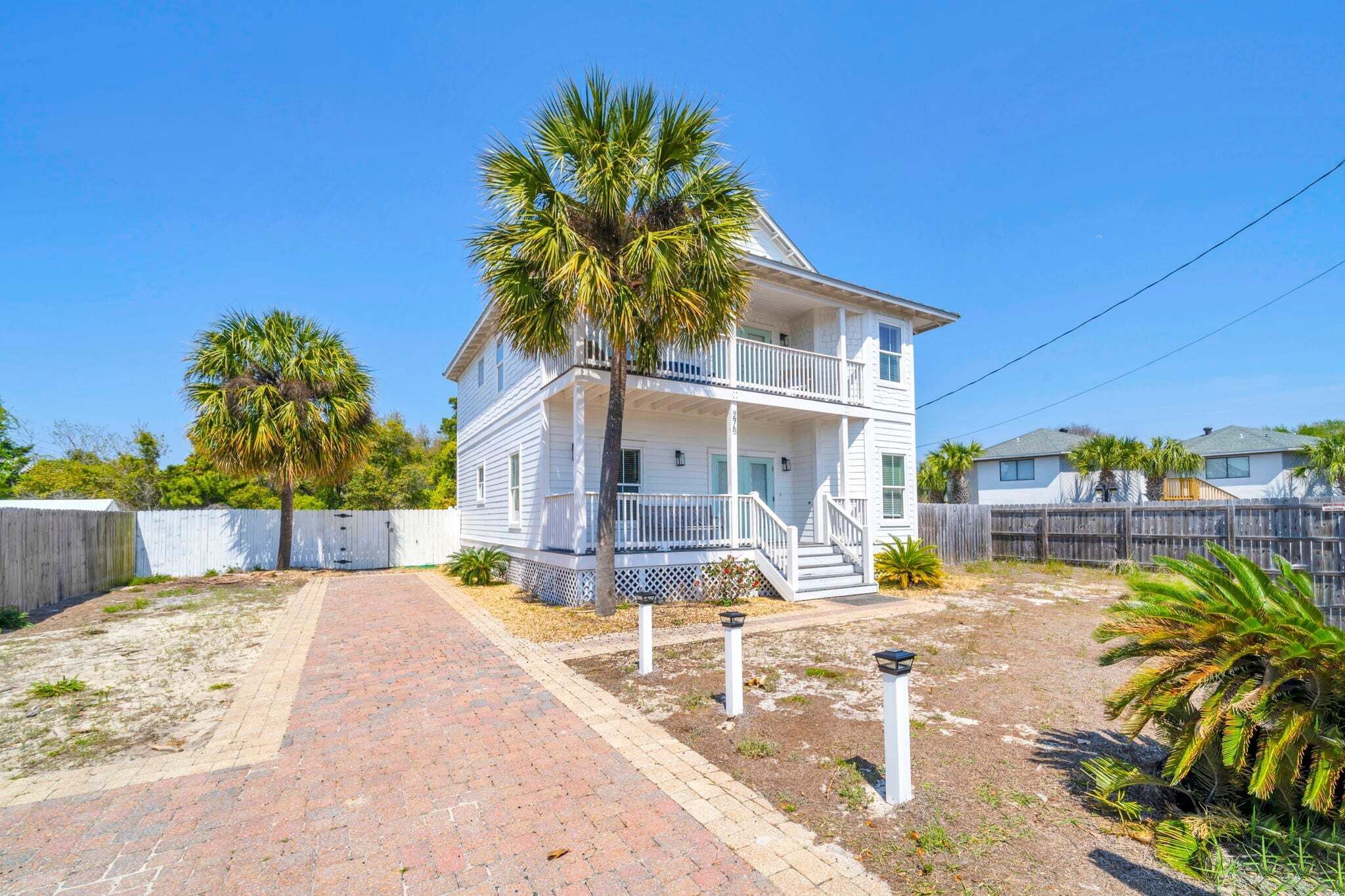 A two-story house with a porch, a palm tree, and a brick pathway.