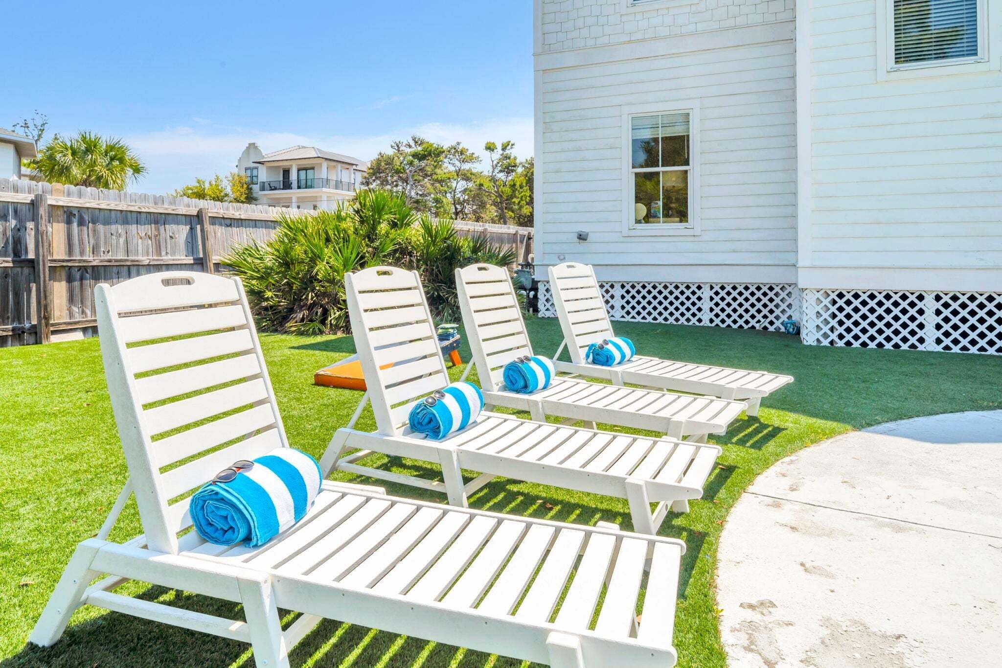 Outdoor lounge chairs with blue towels, a white house, and a wooden fence.