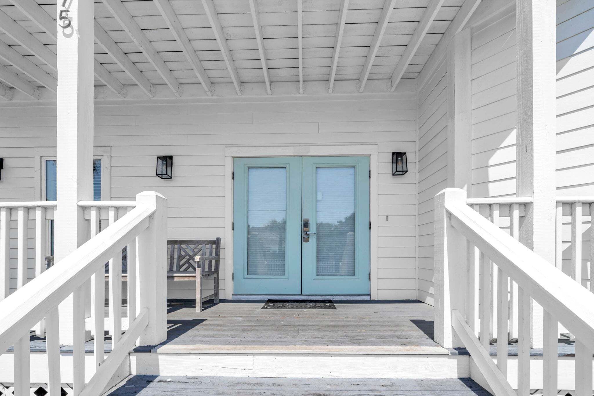 A white porch with a blue door, white railings, and a small table with a chair.