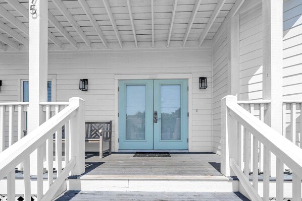 A white porch with a blue door, white railings, and a small table with a chair.