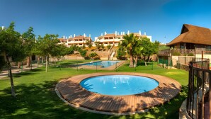 A resort with a swimming pool, a play area, and a building with a thatched roof.