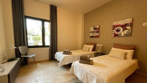 A hotel room with two beds, a desk, a chair, and a window with curtains.