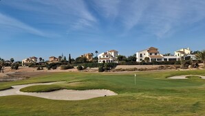 A golf course with sand bunkers, a flag, and houses in the background.