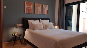 A bedroom with a bed, pillows, a nightstand, a lamp, and wall art.