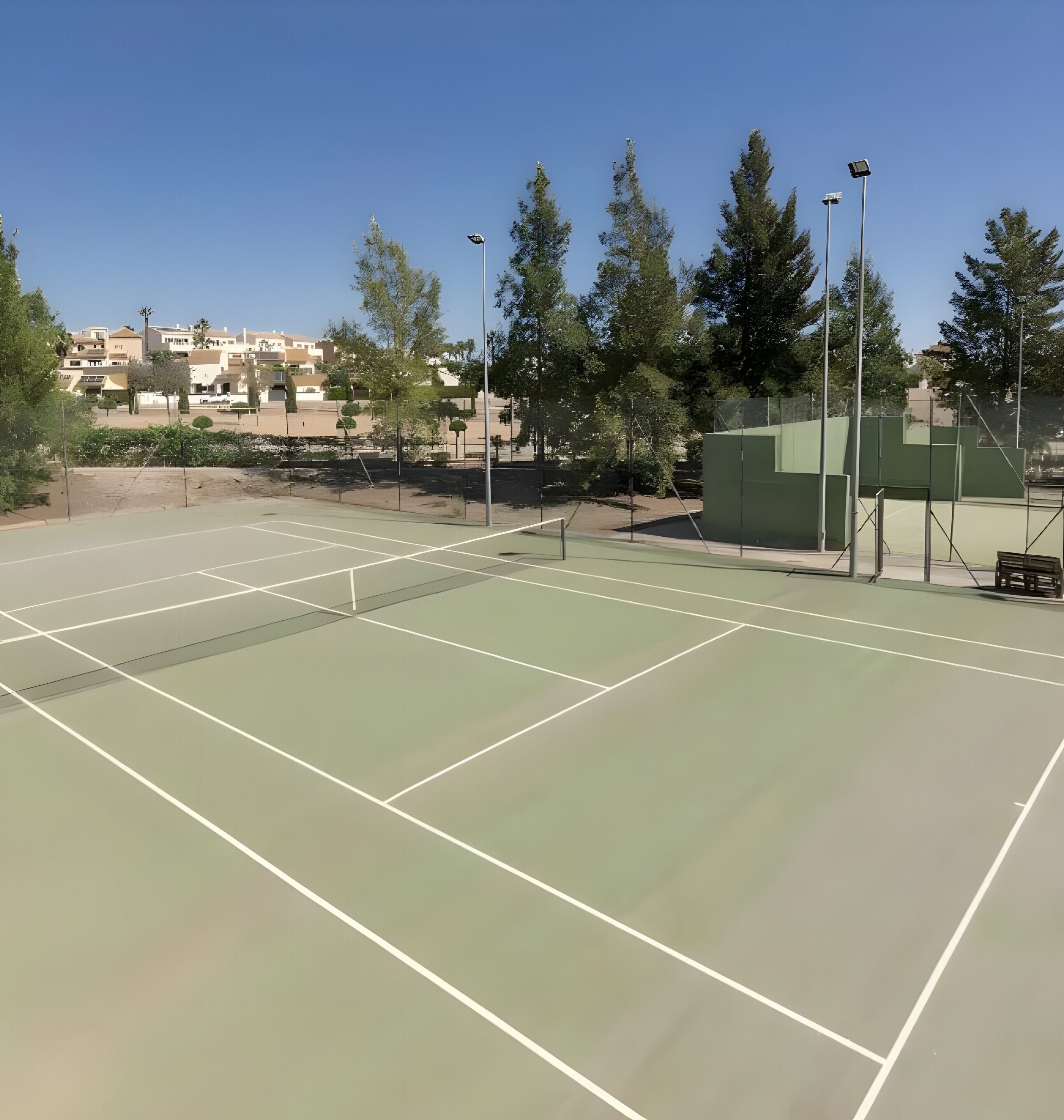 Een tennisbaan buiten met duidelijke lijnen, omgeven door bomen en gebouwen.