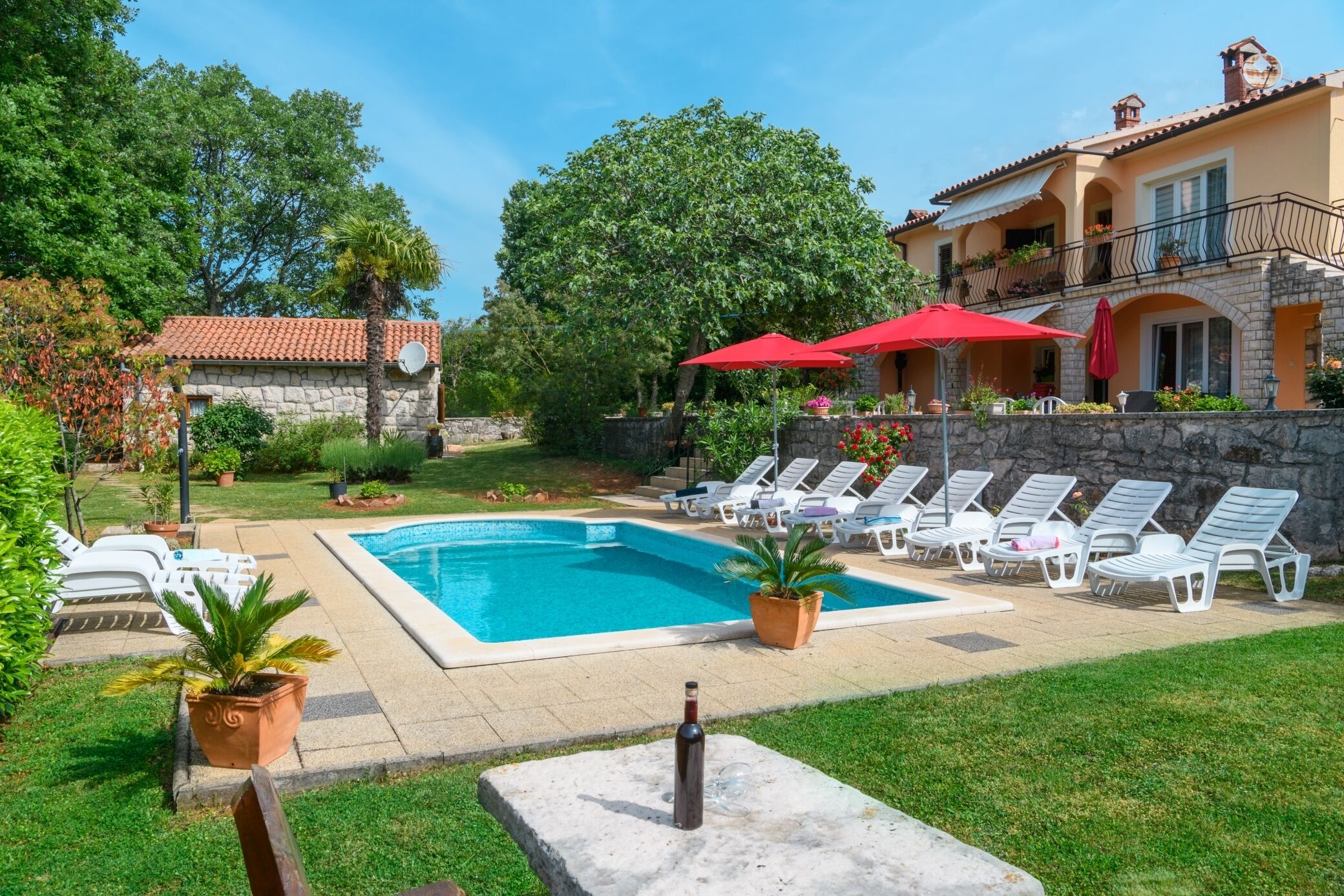 A pool area with lounge chairs and umbrellas, surrounded by greenery and a stone building.