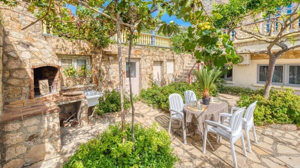 A stone courtyard with a brick fireplace, outdoor seating, and lush greenery.