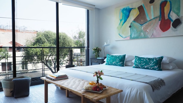 Een moderne slaapkamer met een groot bed, een houten bankje en uitzicht op de omgeving door grote ramen.