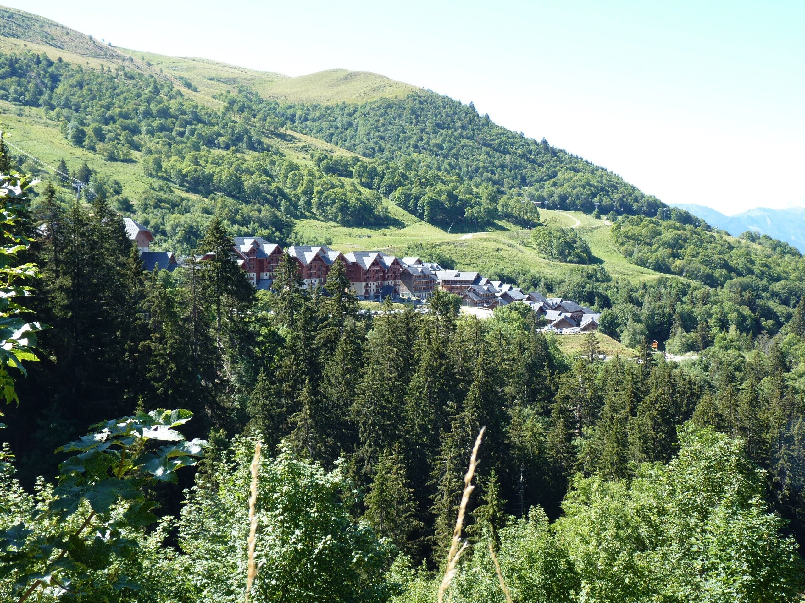Un complejo turístico de montaña con varias construcciones de estilo chalet, rodeado de un bosque frondoso y colinas ondulantes.