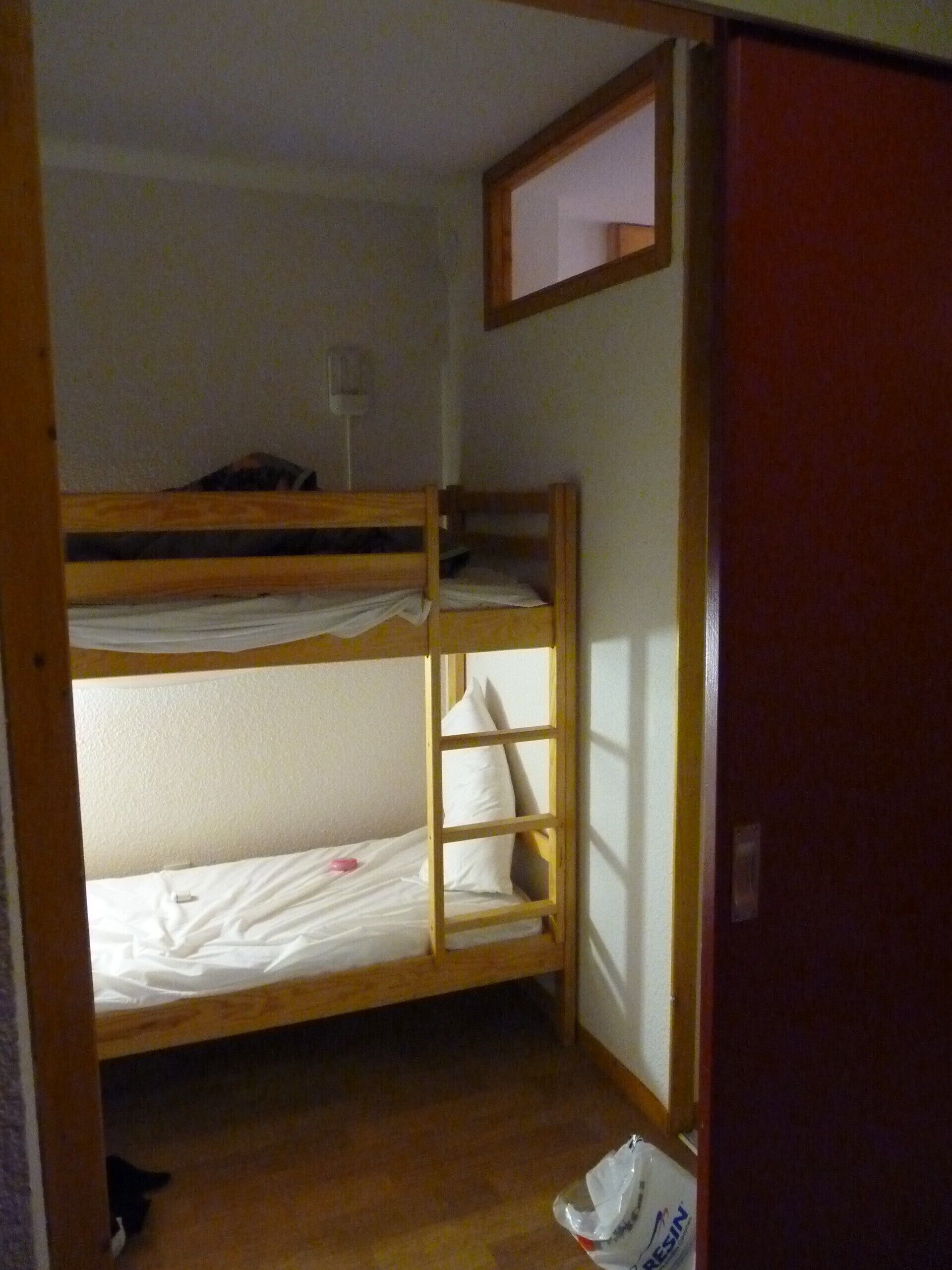 A bunk bed room with a wooden frame, a small window, and a door.